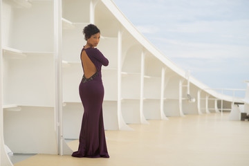 Obraz na płótnie Canvas Beautiful african woman with black hair wearing violet dress posing on the bow of the white ship on the white construction on background
