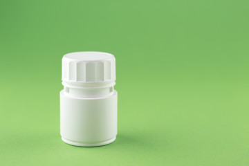 Close up white pill bottle on pistachio green background with copy space. Focus on foreground, soft bokeh. Pharmacy drugstore concept