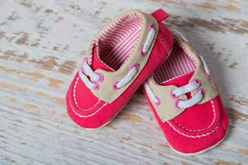 Baby red shoes on a rope against a white brick wall.