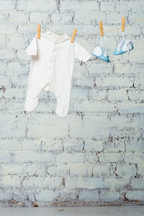 Children's white body and blue shoes on a rope against a white brick wall.