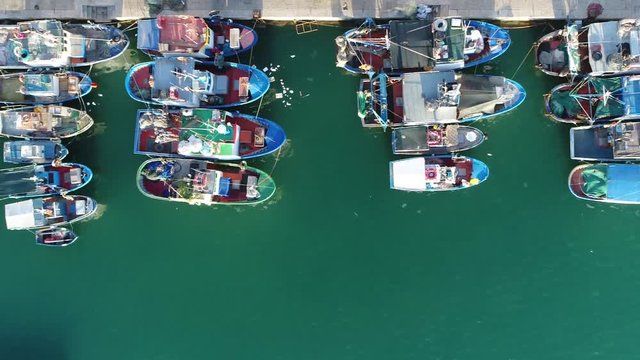 Aerial top-down view of traditional mediterrenean fishing vessels docked in typical italian fishing harbor in Trapani Sicily in Italy looking down onto colorful boats and the azure blue ocean water 4k