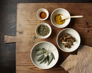 Spices, mushrooms and leaves in white bowls on a rustic wooden cutting board