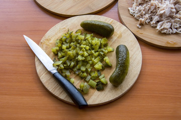 Finely chopped pickled cucumber on the board and a cutting knife; Boiled chicken, onions on the wooden table top