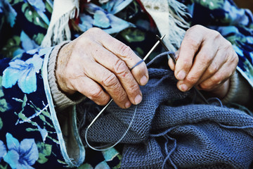 Knitting needles with knitting thread in old wrinkled hands of the mother close-up
