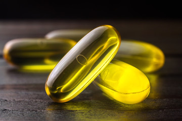 Yellow capsules omega 3, fatty acid, fish oil on dark wooden table, macro image