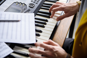 Close up of pianist hands playing on synthesizer. Notes are on musical instrument. Top view