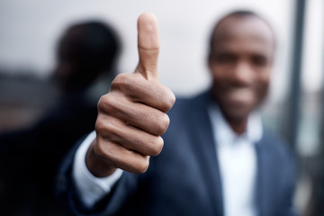 Its OK. Close-up of african businessman hand is showing thumb up while expressing gladness. He is standing outdoors. Focus on hand
