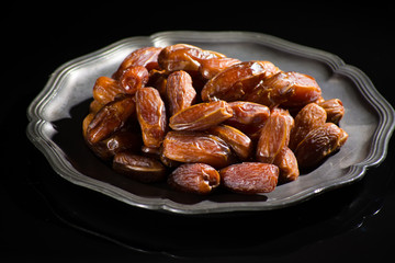 Sweet dessert dried date in old tin bowl, low key, dark theme, on black background with reflection