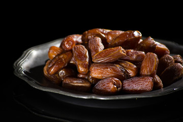 Sweet dessert dried date in old tin bowl, low key, dark theme, on black background with reflection