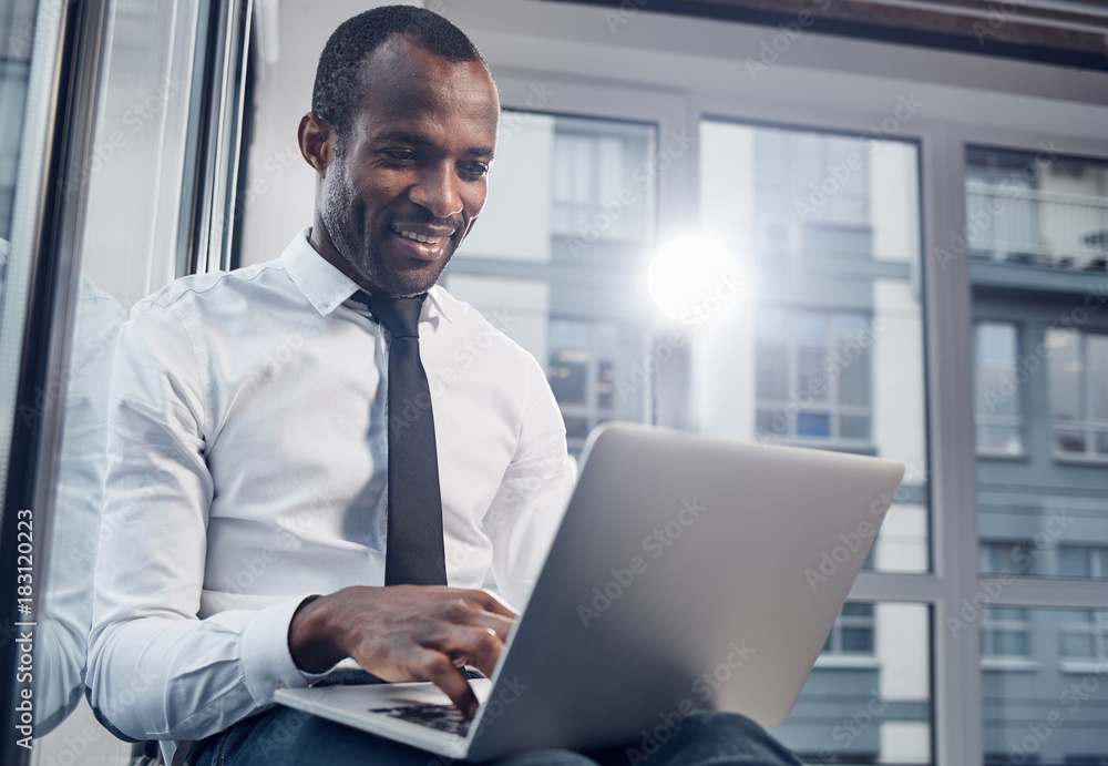 Poster daily life. low angle of delightful stylish young african businessman is smiling while sitting on wi