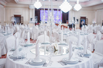 The crystal and glass candelabrum stands in the middle of the festive table at the banquet. The candles burn on it.