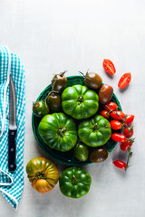 ingredients for salad from different types of tomato on a white stone table. cutting board, olive oil and condiments. healthy food, summer or spring menu