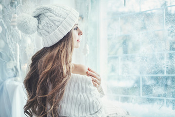 Indoor portrait of young beautiful girl wearing knitted winter beanie hat and dress. Model looking...