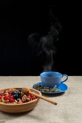 herbal tea and honey with honeycomb in a wooden bowl with red currants and blueberries or blueberry on a background of a linen tablecloth