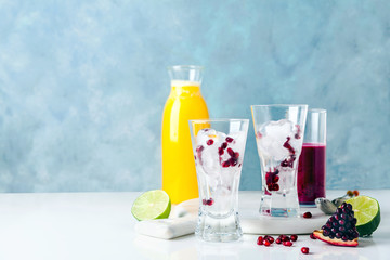two glasses with ice and pomegranate seeds, ready for cocktails. Freshly squeezed pineapple and pomegranate juices and halves of cut lime in the background.
