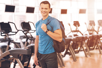 Fototapeta na wymiar A young man is posing in the gym. A muscular man in a blue T-shirt is smiling.