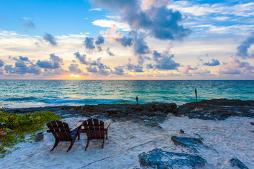 Fototapeta na wymiar Sunset at paradise beach - Chairs under the palm trees on beach at tropical Resort. Riviera Maya - Caribbean coast at Tulum in Quintana Roo, Mexico