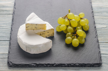 Камамбер с виноградом на каменной доске черного цвета