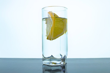 A slice of lemon in a glass of water on light background