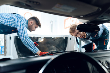 Obraz premium Father and son work at the auto service. Two mechanics work with the details of the car.
