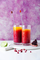 cocktail Tequila Sunrise on white table and bright pink background. pomegranate seeds and halves of cut lime. Modern classic