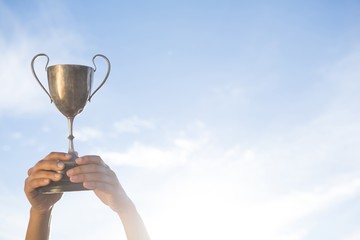 Hand holding a trophy against sky and cloud