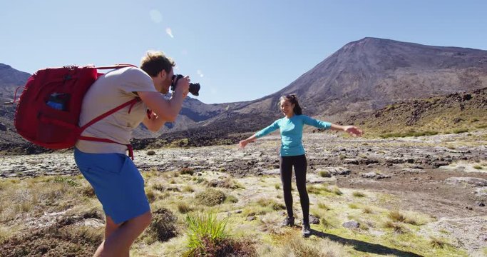 Travel Lifestyle Couple - Man Photographing Happy Woman in New Zealand by Mount Ngauruhoe mountain volcano. Male and female hikers hiking in Tongariro Alpine Crossing National Park.