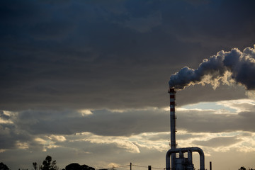 Smoking Red and White Bands Chimney On Backlight With White Smoke At Sunset