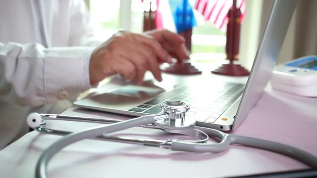 Doctor's writing and working on laptop computer, writing prescription clipboard with record information paper folders on desk in hospital or clinic, Healthcare and medical concept. Focus stethoscope