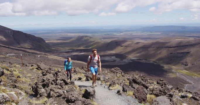 Young man and woman hiking wearing backpacks walking in amazing volcanic landscape in New Zealand. Couple backpackers hiking in Tongariro National Park. Stunning landscape, Tongariro Alpine Crossing.