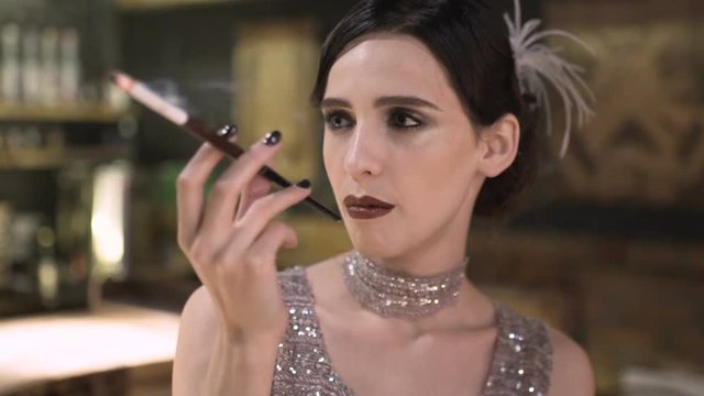 portrait of a young attractive woman in a 1920s style smoke cigarette at the bar. Model with a beautiful make-up
