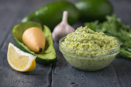 Bowl with cream of avocado, a slice of lemon, garlic and herbs on wooden rustic table.