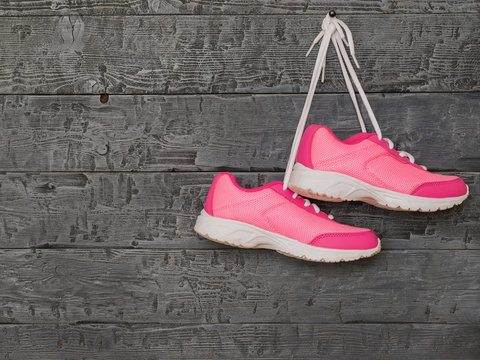 Pair pink womens running shoes hanging by the laces on the wooden wall.