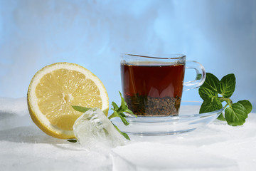 glass cup of strong black tea on a beautiful blue ice with yellow lemon and green mint