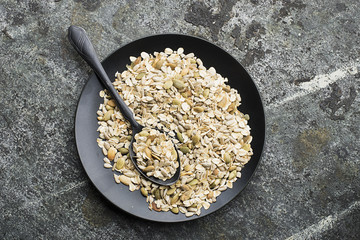 Ingredients for the preparation of baked crispy appetizing toping for thick soups puree from pumpkin seeds, sunflower seeds, oat flakes in ceramic form on a dark background. Top View.