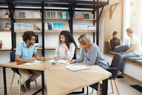 People working in team. Three young perspective business partners sitting in library discussing on startup project details and profits. Teamwork concept.