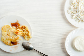 White plates with curd pancakes, soft cheese, fresh curd are standing on white wooden table and copy space.