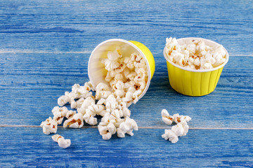 Falling popcorn in yellow paper box on a blue wooden background