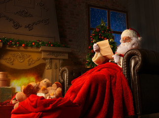 Portrait of happy Santa Claus sitting at his room at home near Christmas tree and reading Christmas...