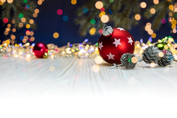 red glass ball with pine cones on white wooden background against blurry holiday lights