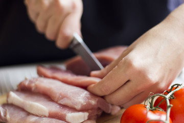 Obraz premium Closeup of the hands of a butcher cutting slices of raw meat off a large loin