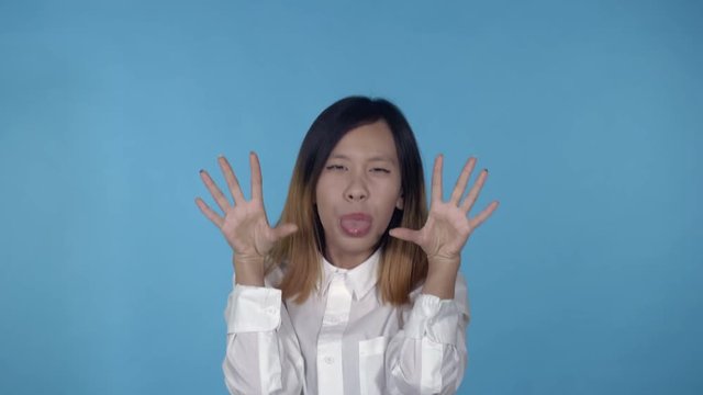 young asian woman posing have fun making faces on blue background in studio. attractive millennial girl wearing white casual shirt looking at the camera smiling