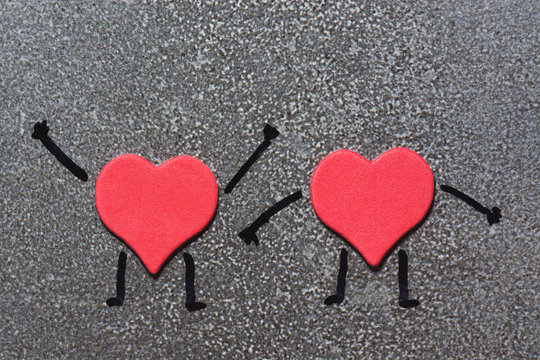 Two red hearts resembling a man with painted hands and feet on a gray background. Valentine's Day. Funny hearts.