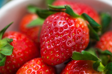Bowl with fresh strawberry on blue wooden table.