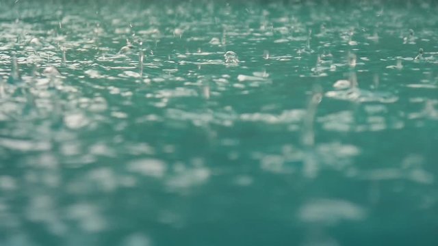 Raindrops fall into the water. Beautiful pool water surface under the rain. Slow motion