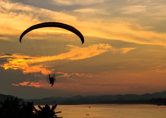 silhouette flying paramotor over river and sunset sky