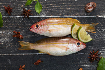 Row of fresh fish with vegetables on black wooden background,concept cooking background.
