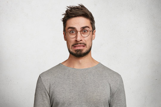 Worried indignant bearded male can`t understand something, has puzzled expression, wears casual clothes and spectacles, isolated over white background. Human facial expressions and feelings.