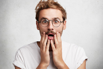 Shocked stupefied male model has trendy hairstyle, mustache and stubble, being in stupor as hears...