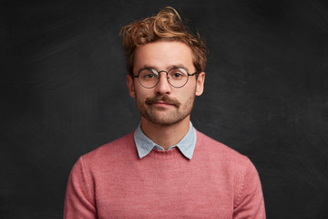 Horizontal shot of confident pleasant looking intelligent male nerd wears elegant clothes, round optical spectacles, poses against chalk blackboard, prepares for presenting information to audience - obrazy, fototapety, plakaty